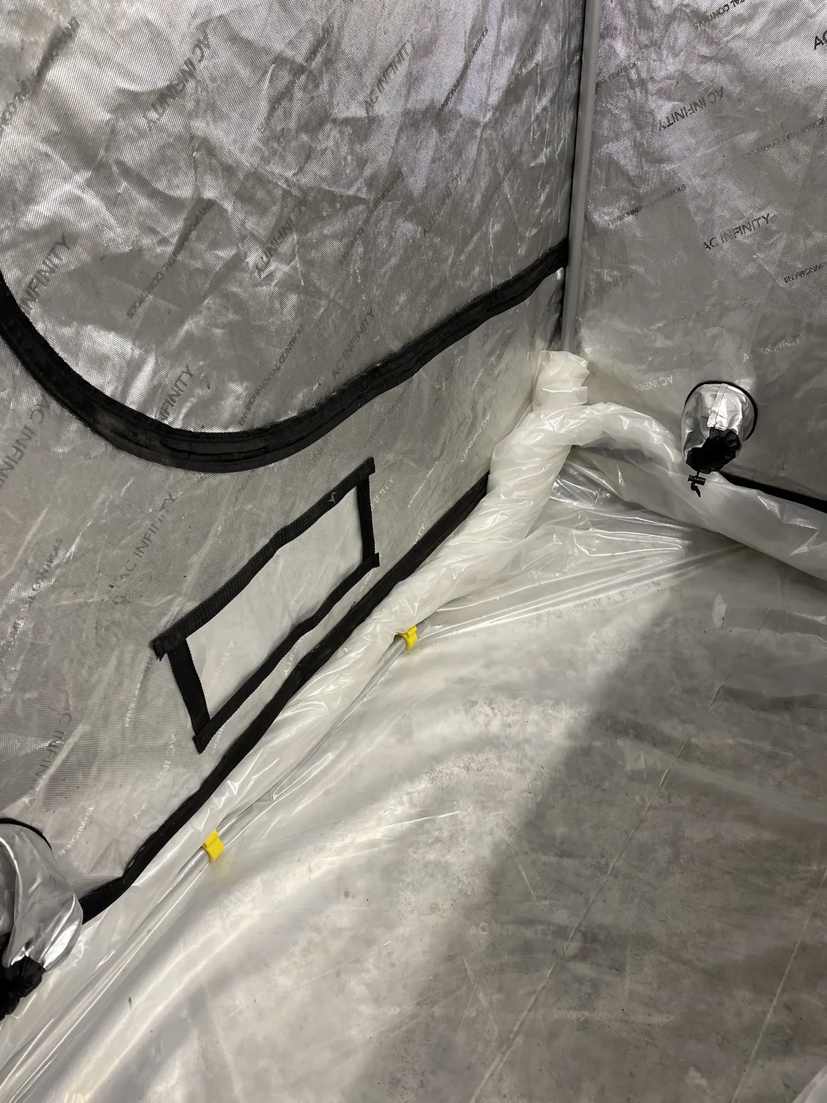 A corner of the tent floor liner, bunched along the base of the wall, with yellow clips on the lower frame tube.