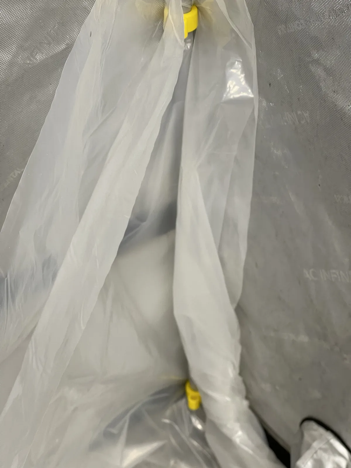 A closer look at the liner with a yellow clip near the top and another near the bottom, the plastic hanging in loose folds between them.