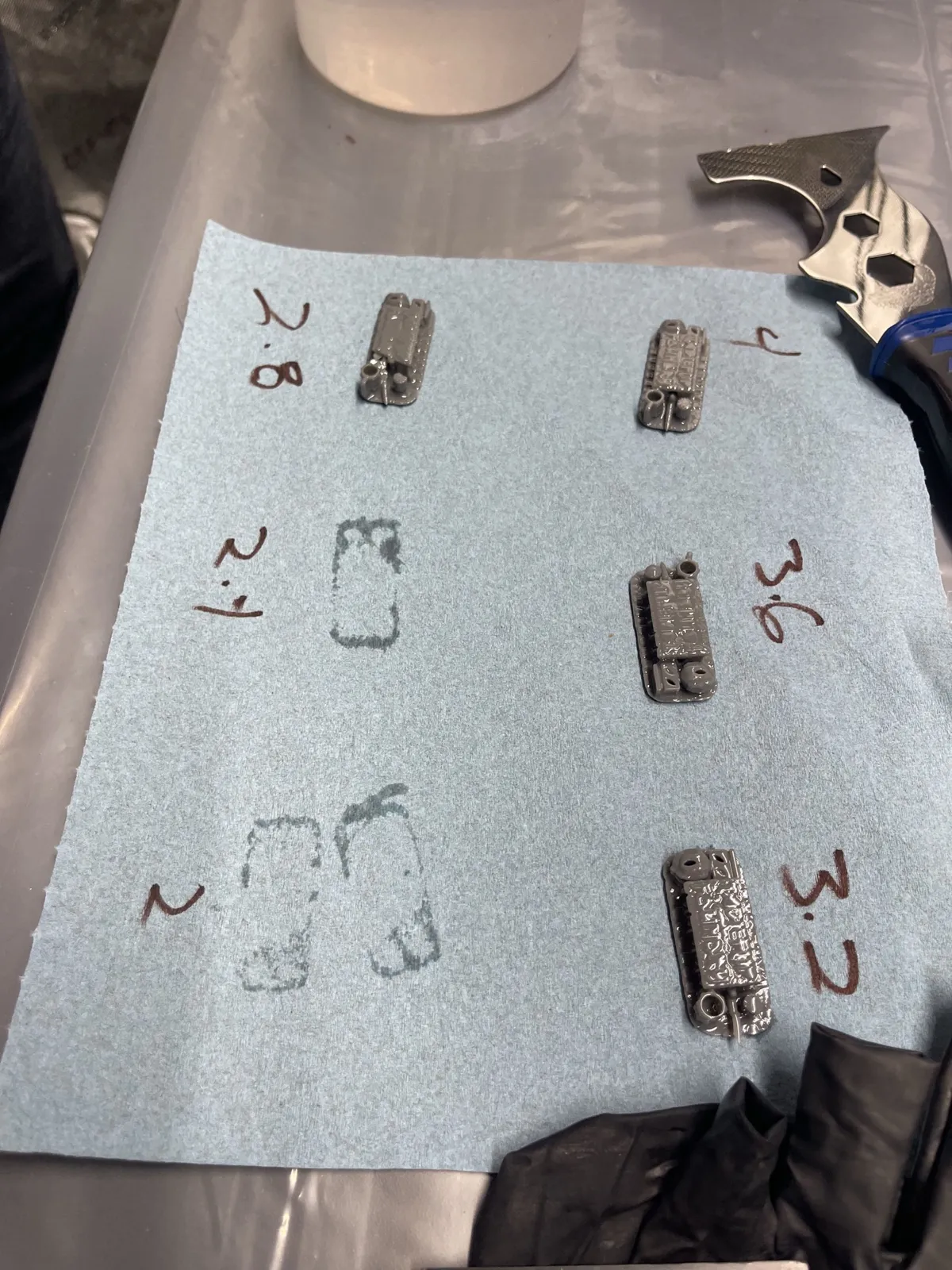 The exposure test pieces on a blue shop towel, labeled 2, 2.4, 2.8, 3.2, 3.6, and 4. The 2 and 2.4 pieces had already moved to the curing station, so only their resin marks are left on the towel.